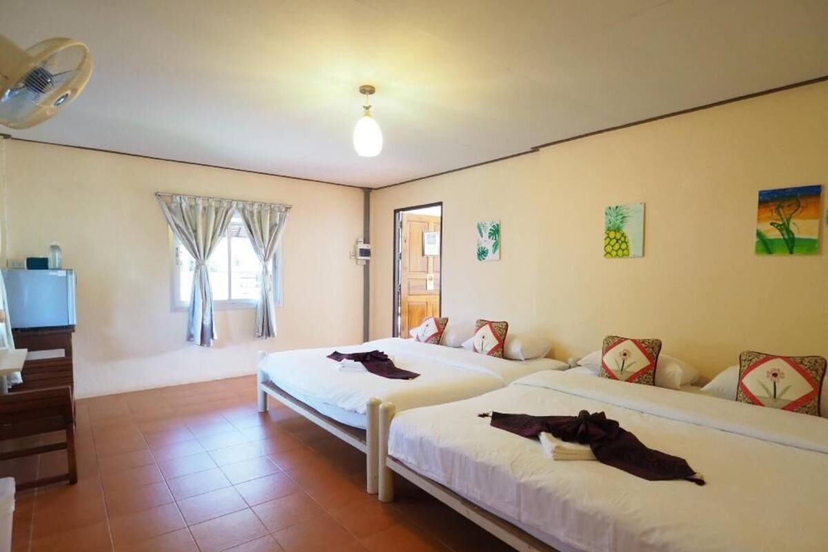 A room with two beds, a desk, a chair, a window with curtains, and a ceiling fan.