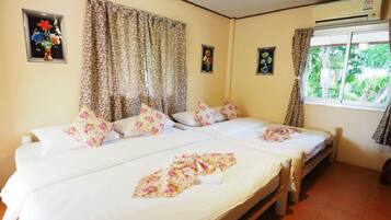 Una habitación con dos camas, ropa de cama estampada con motivos florales, una ventana con vistas a zonas verdes y un aire acondicionado instalado en la pared.