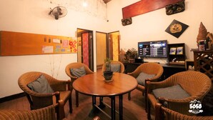 Una habitación acogedora con sillones de mimbre alrededor de una mesa de madera, un tablón de anuncios y un televisor sobre un mueble de madera.