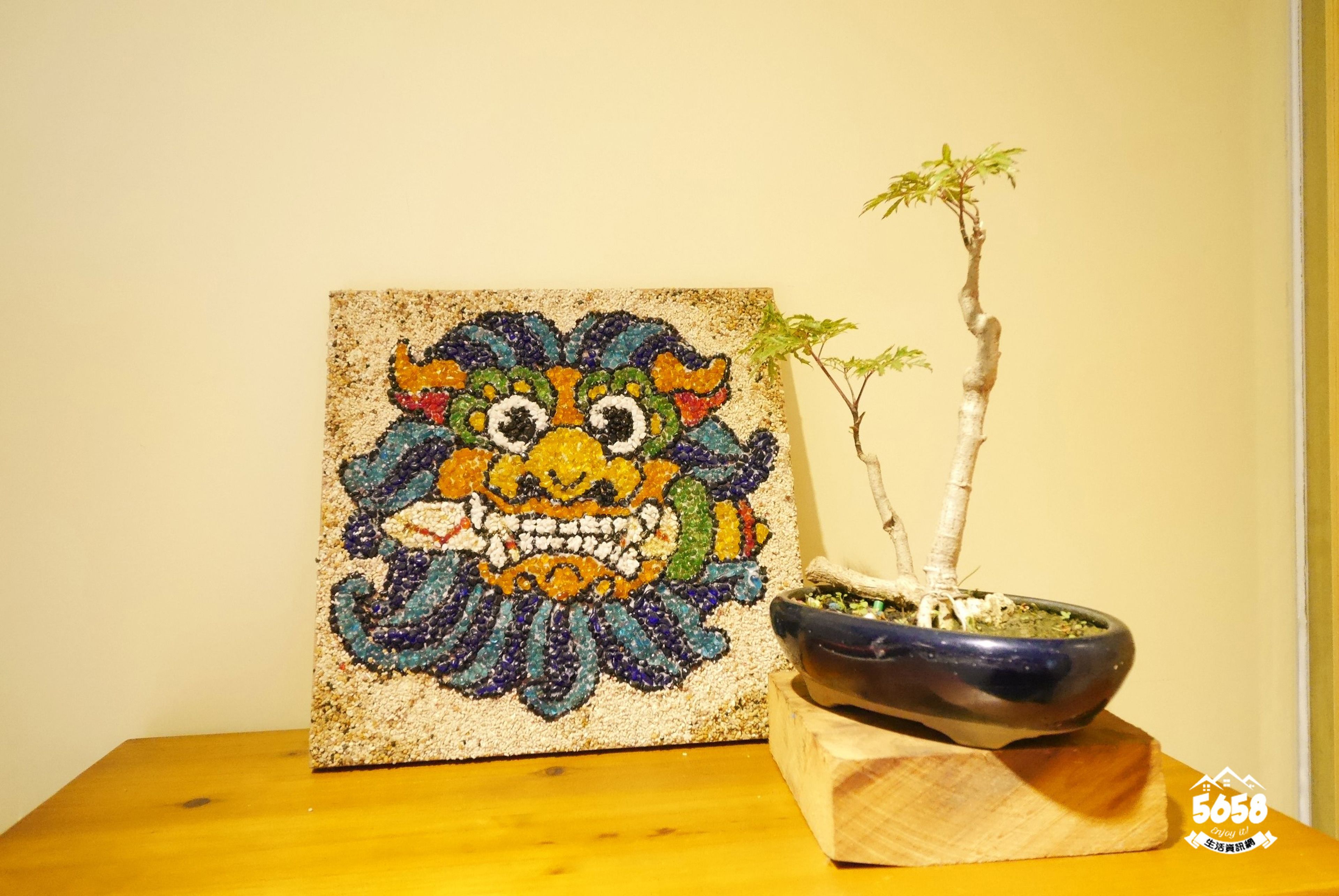 Une mosaïque aux couleurs vives et un bonsaï sur une table en bois.