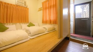 Una habitación con dos camas, cortinas naranjas, suelo de madera y una puerta con reja de metal.