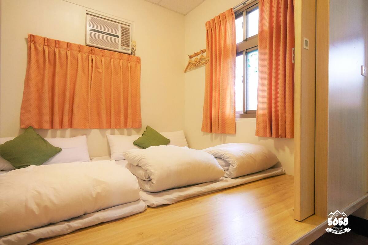 Une chambre avec deux lits, des rideaux orange, une fenêtre et un climatiseur fixé au mur.