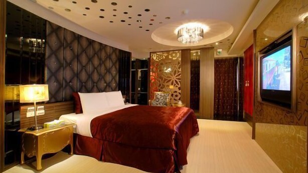 A hotel room with a large bed, a TV, a chandelier, and a decorative wall panel. - WE Motel (Kaohsiung)