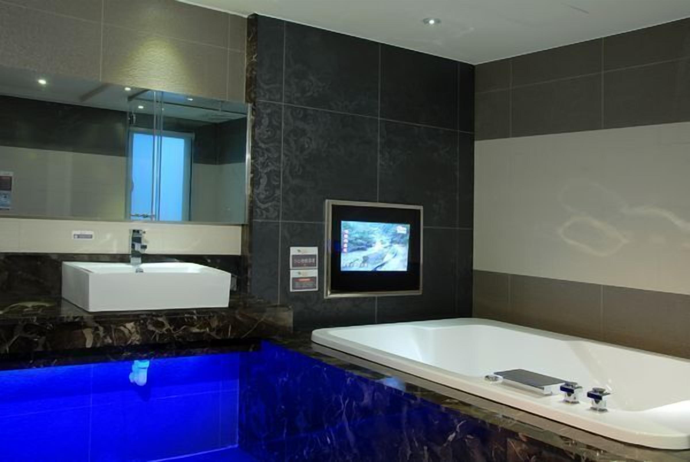 A modern bathroom with a marble countertop, a white sink, a large bathtub, and a wall-mounted TV.