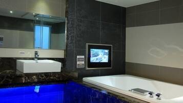 A modern bathroom with a marble countertop, a white sink, a large bathtub, and a wall-mounted TV.