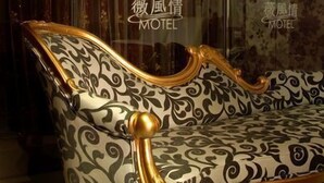 A room with a patterned sofa, a chandelier, and a wall with a floral design. - WE Motel (Kaohsiung)