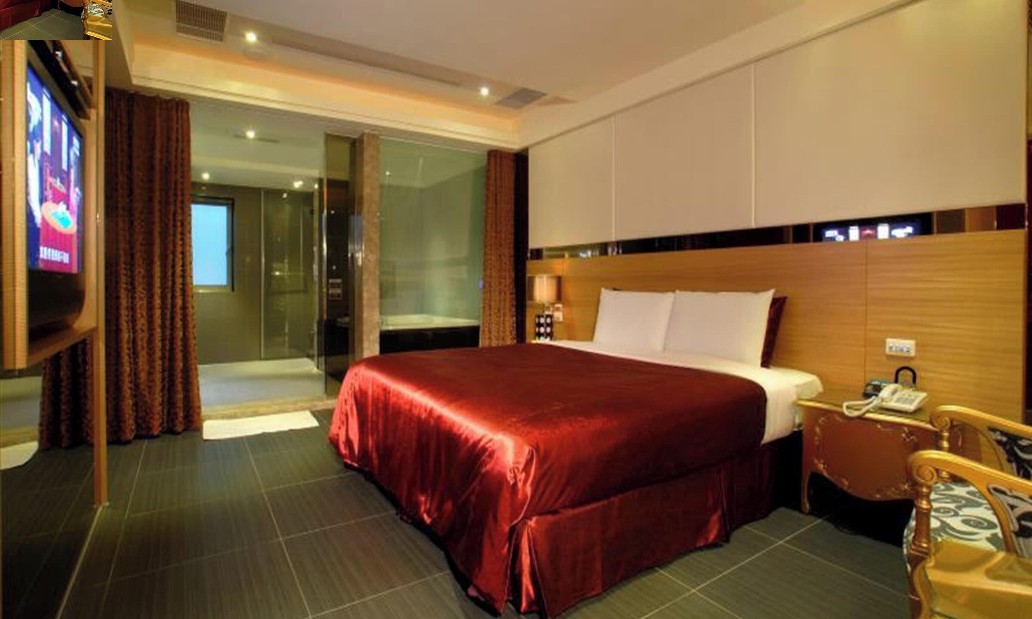 A hotel room with a large bed, a television, a desk with a telephone, and a chair.