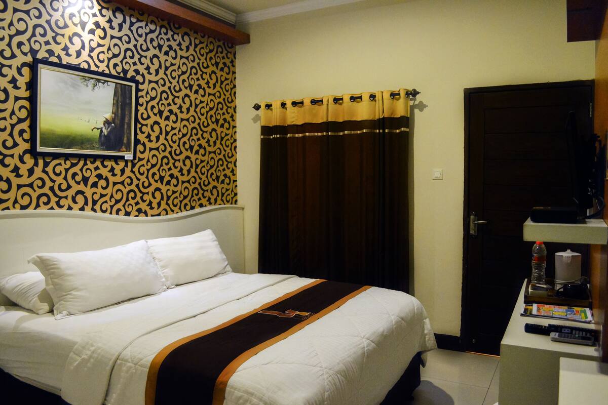 A hotel room with a bed, a picture on the wall, a curtain, and a door.