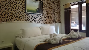A hotel room with a bed, pillows, a blanket, a wall with a decorative pattern, a framed picture, and a window with curtains. - Kabana Hotel (Mataram)