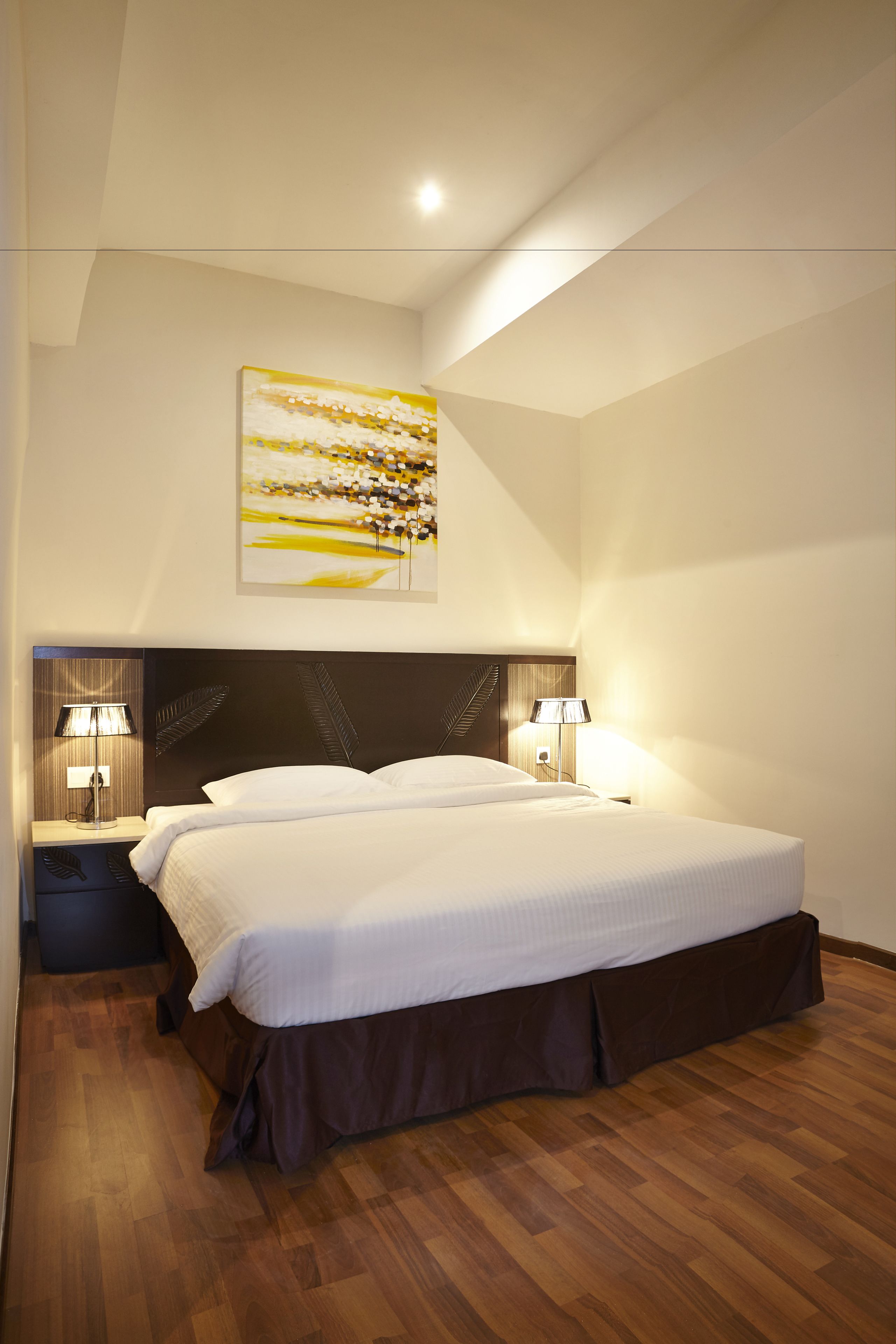Ein Hotelzimmer mit einem großen Bett, zwei Nachttischen mit Lampen, einem Holzboden und einer Deckenleuchte.