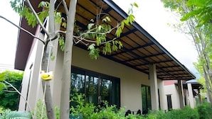 A modern house with a covered patio, surrounded by lush greenery and a well-maintained garden. - Charming in Khao Yai Hotel (Pak Chong)