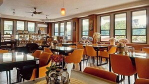 A spacious dining area with high ceilings, large windows, and modern orange chairs. Tables are set with clear glassware and decorative flowers. - Charming in Khao Yai Hotel (Pak Chong)
