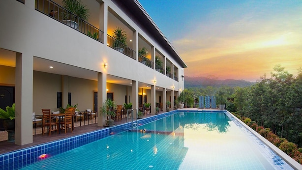 A modern hotel with a large outdoor swimming pool, multiple balconies with plants, and a view of the surrounding landscape. - Charming in Khao Yai Hotel (Pak Chong)