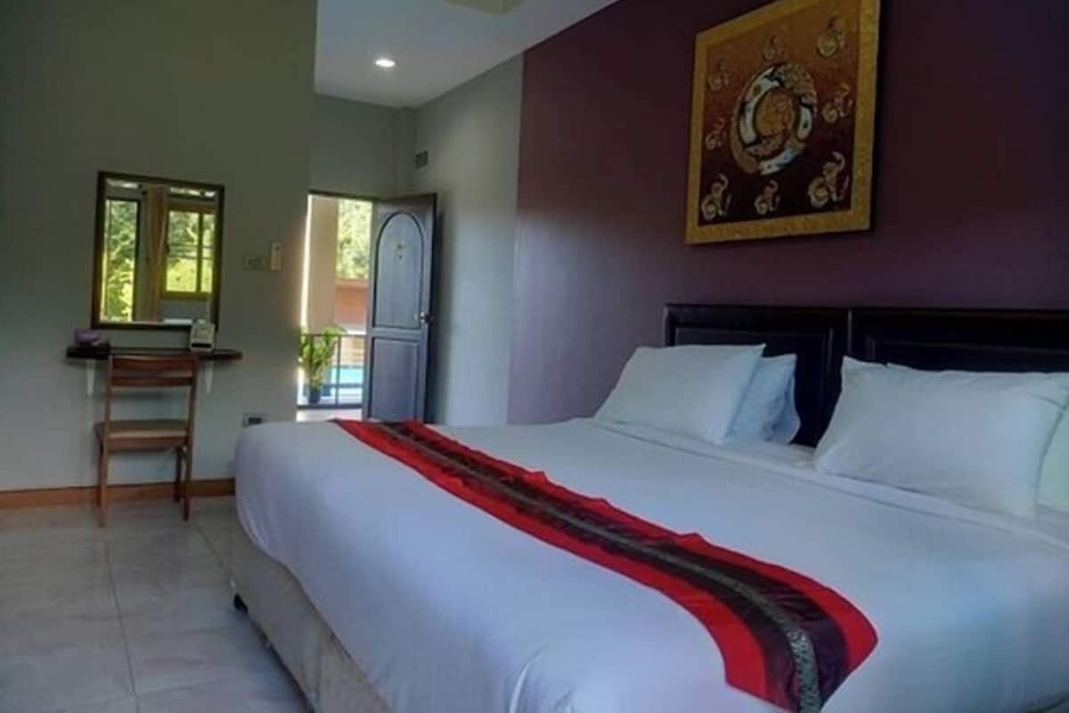 Ein Hotelzimmer mit einem großen Bett, einem Schreibtisch mit Stuhl, einem Fenster und einer zur Außenseite führenden Tür.