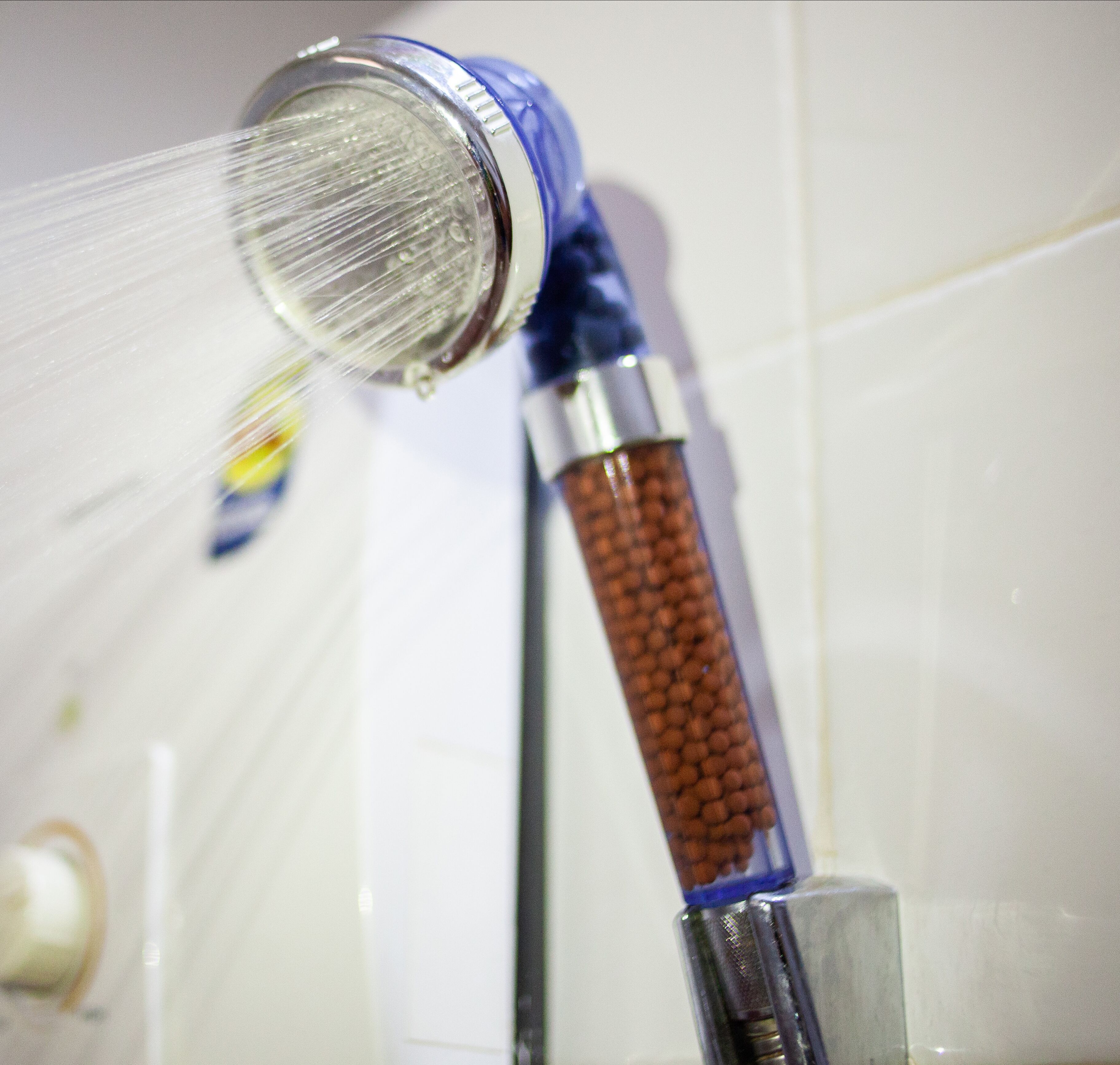 Um chuveiro com um jato de água transparente, um puxador de madeira e uma base metálica.