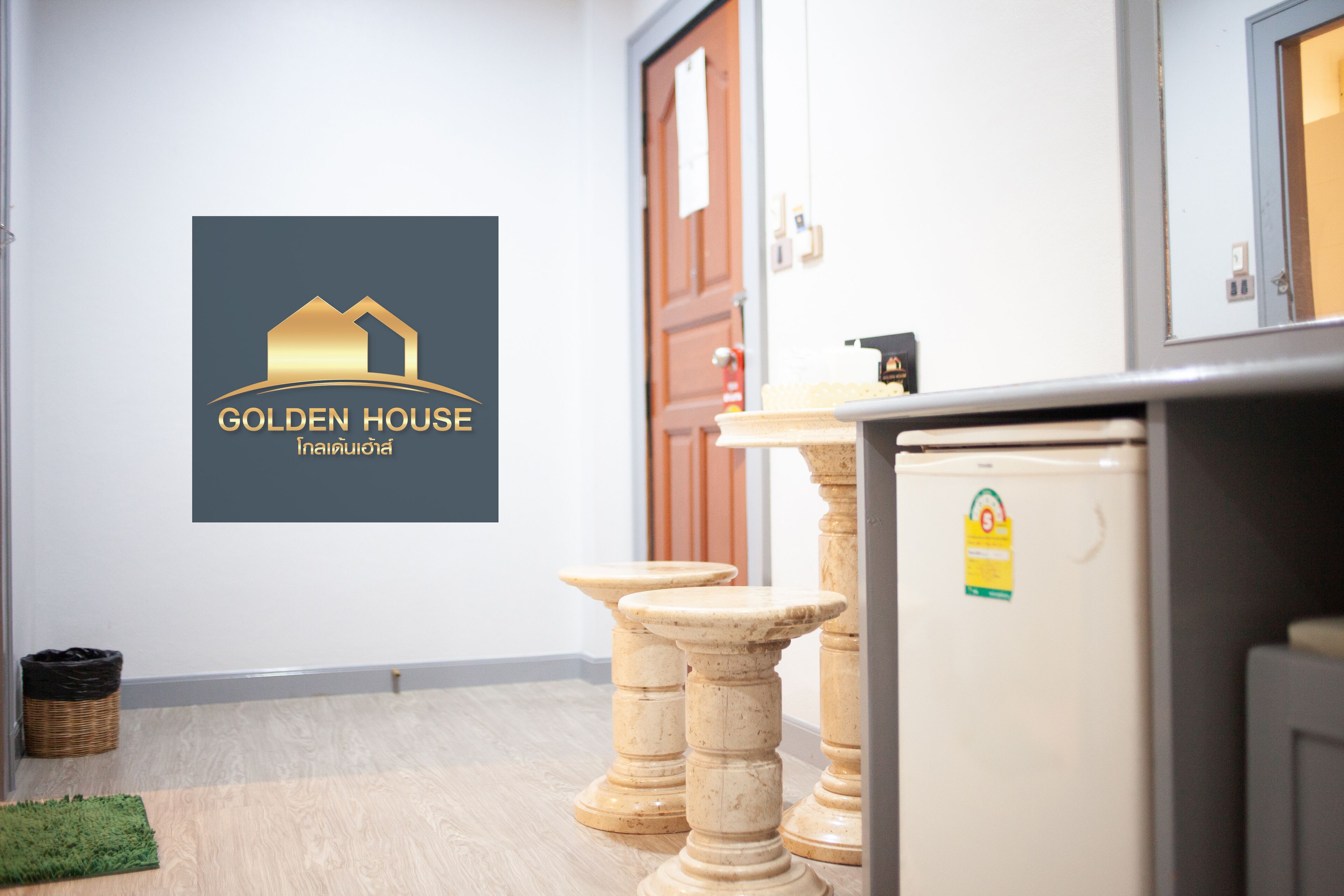 Habitación de hotel con un logotipo en la pared, un refrigerador y un taburete de madera.