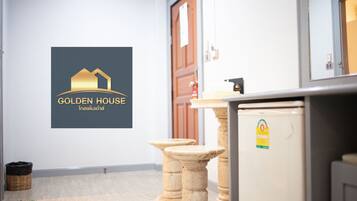 Habitación de hotel con un logotipo en la pared, un refrigerador y un taburete de madera.