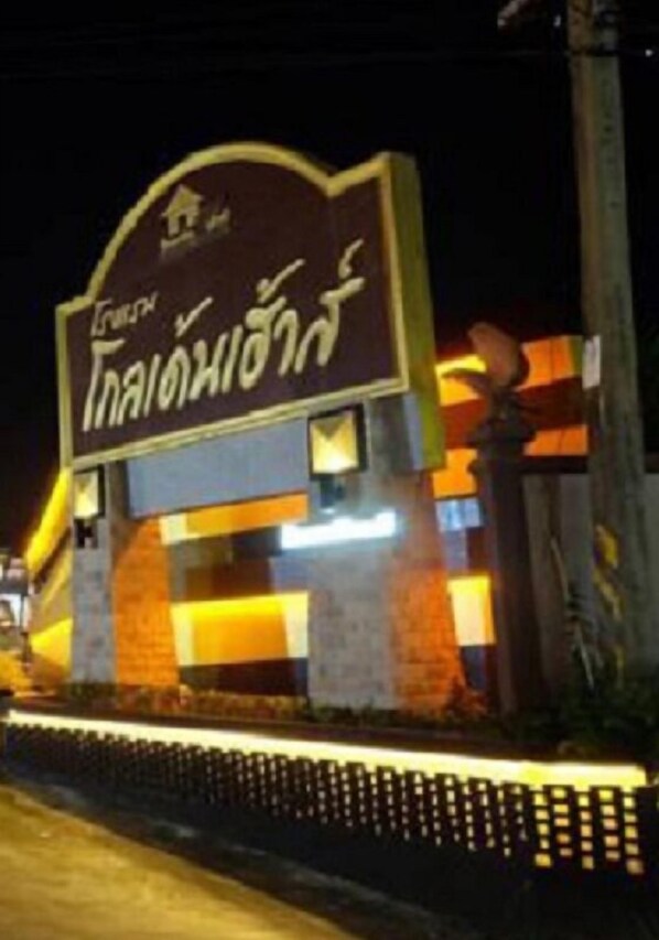 A hotel entrance with a sign in a foreign language, a brick facade, and a well-lit pathway. - Golden House Hotel Sakaeo (Sa Kaeo)