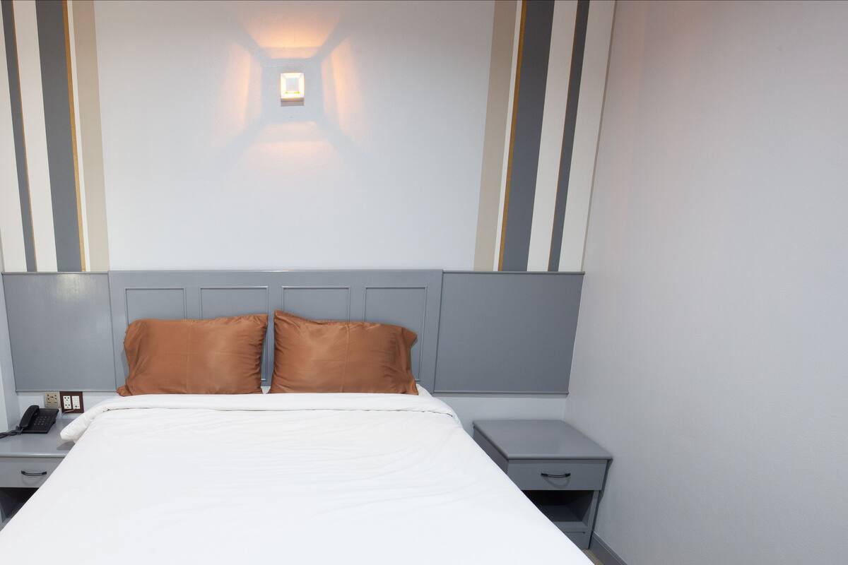 Une chambre d’hôtel moderne avec un grand lit, deux tables de chevet, une lampe de chevet et un luminaire fixé au mur.