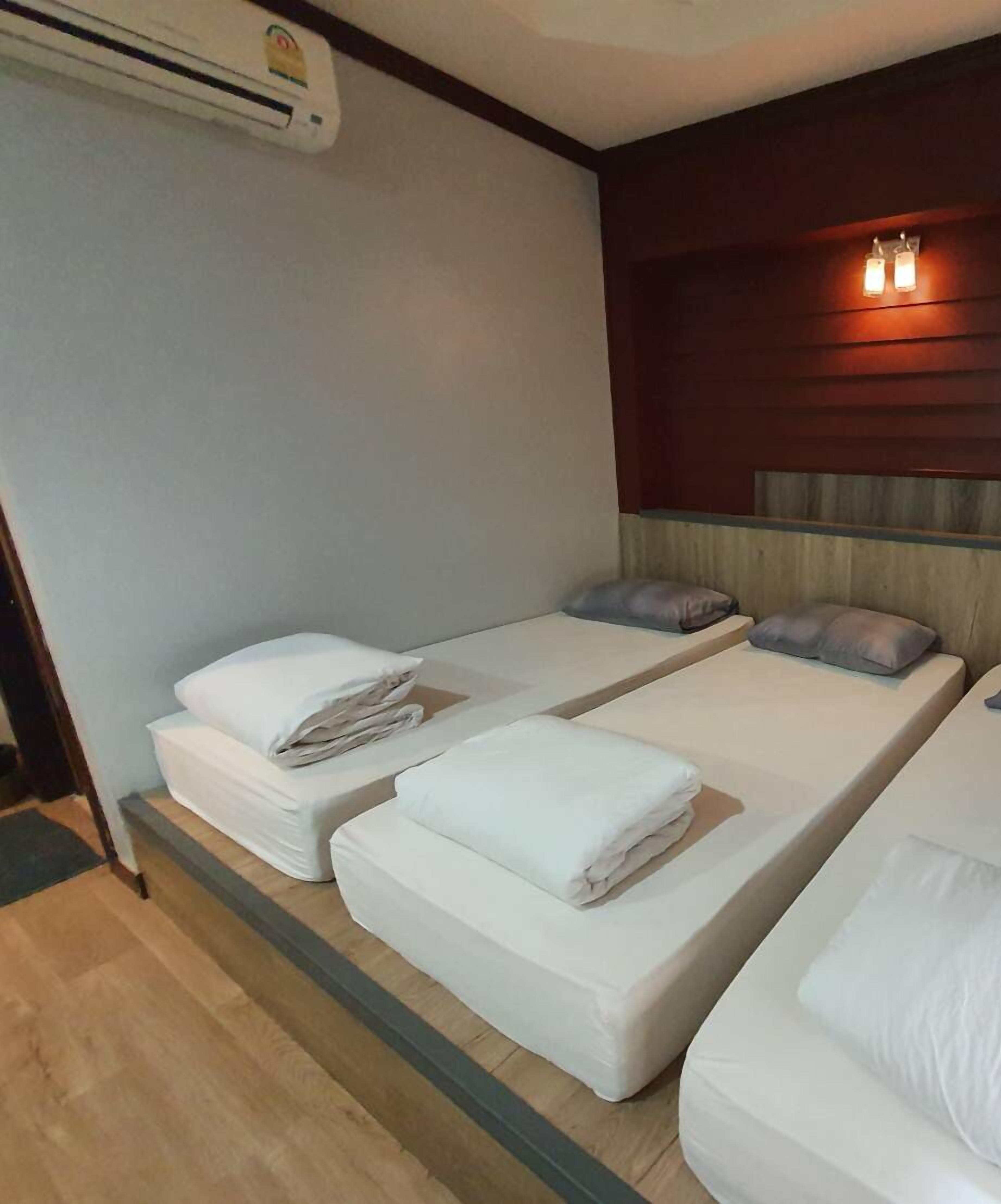 A hotel room with two single beds, a wooden headboard, a wall-mounted air conditioner, and a small window with curtains.