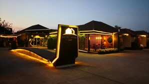 Een hotelentree met een modern verlicht bord, een overdekt terras en een gebouw met een pannendak.