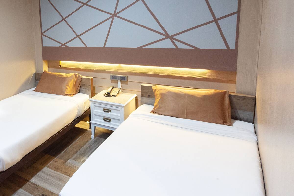Une chambre d’hôtel avec deux lits, une table de chevet avec un téléphone et un mur orné d’un motif géométrique.