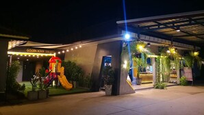 Het uiterlijk van Golden House Sakafon, met een speelruimte voor kinderen inclusief een glijbaan en een overdekt entreegebied met plantenbakken en terrasmeubilair.