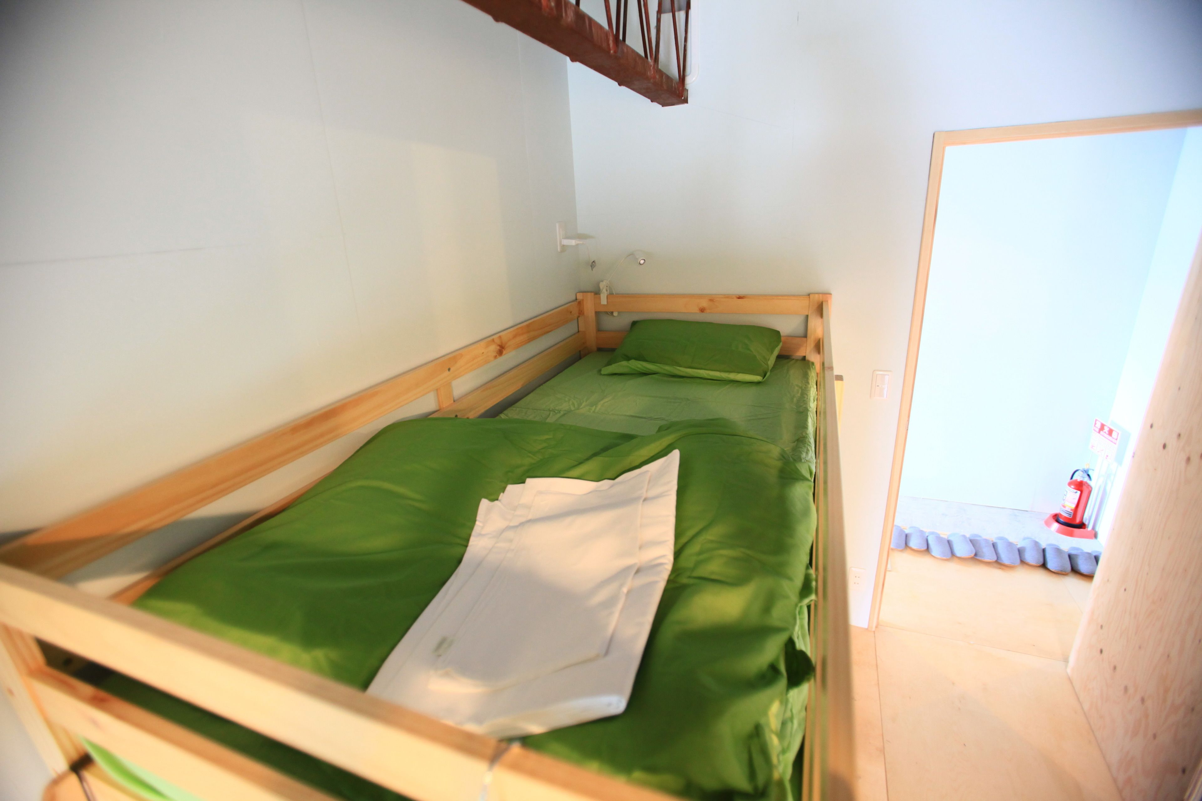 Ein kleines Zimmer mit einem Einzelbett, Holzrahmen, grüner Bettwäsche und einem weißen Kopfkissen.