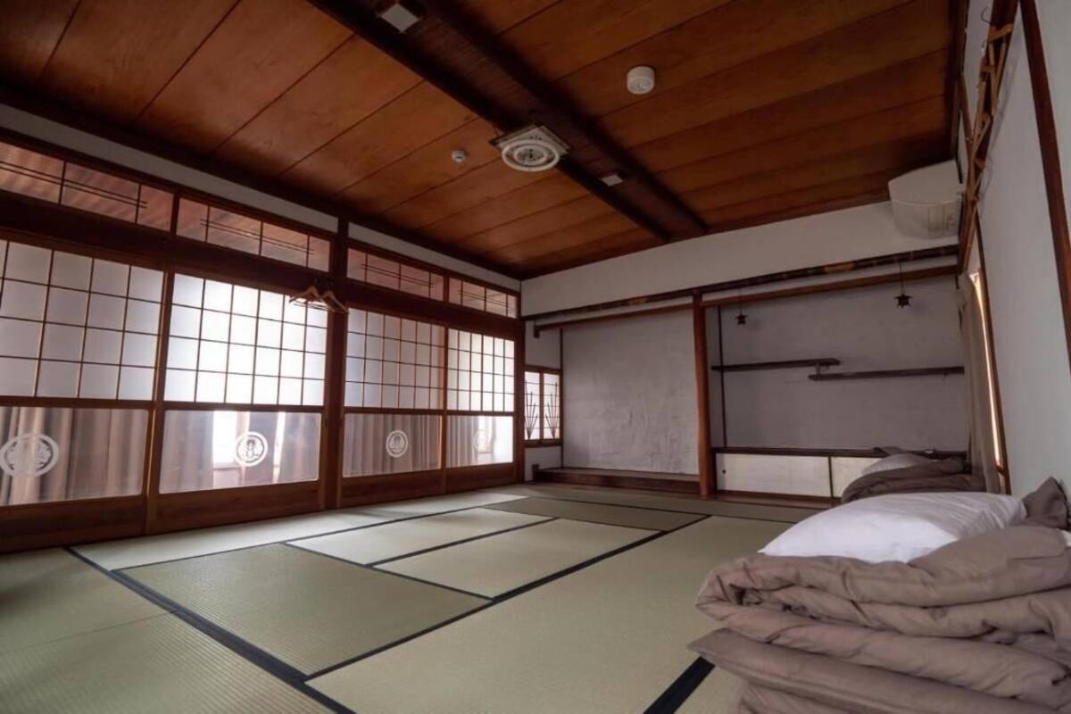 A traditional Japanese room with tatami flooring, sliding doors, and a bed with a white mattress and brown bedding.