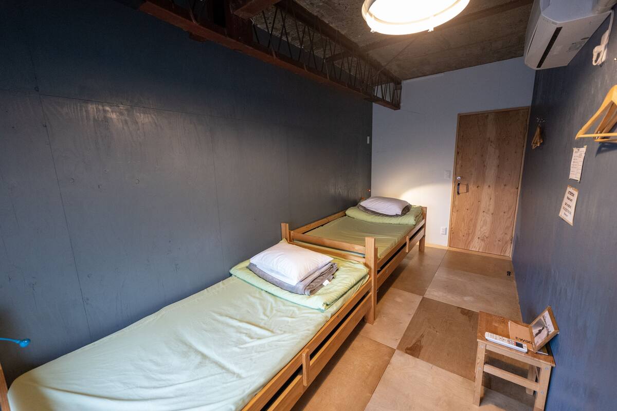 A small, compact room with two wooden bunk beds, a small table with a remote control, and a door leading to another room.