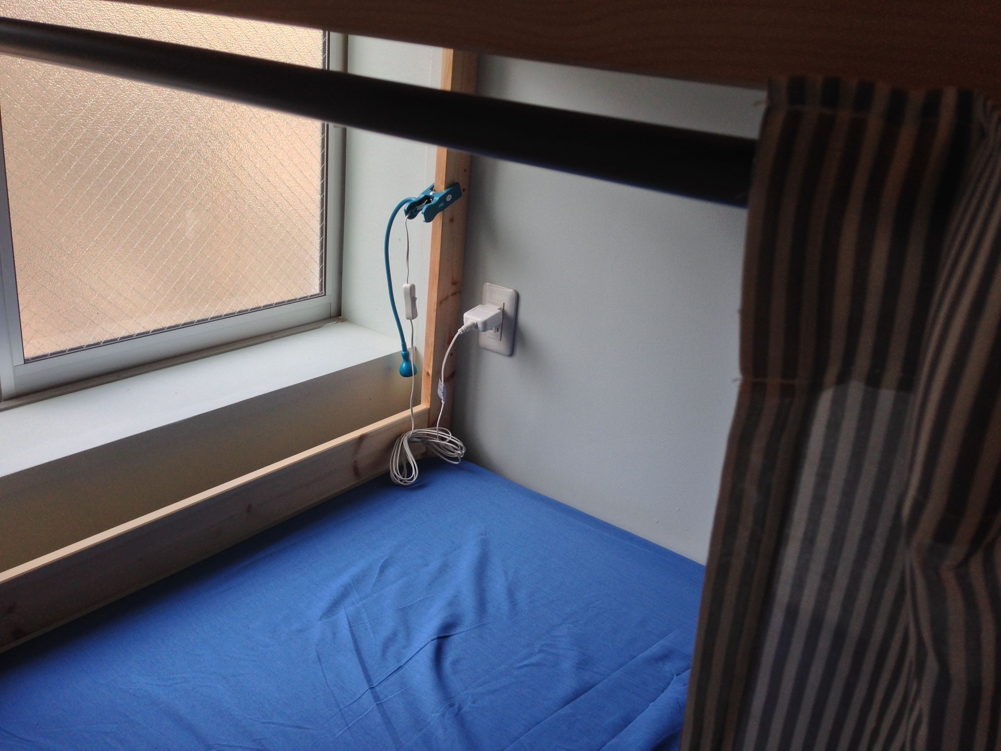 Een kleine kamer met een enkel bed, een raam, een stopcontact en een blauw matras.