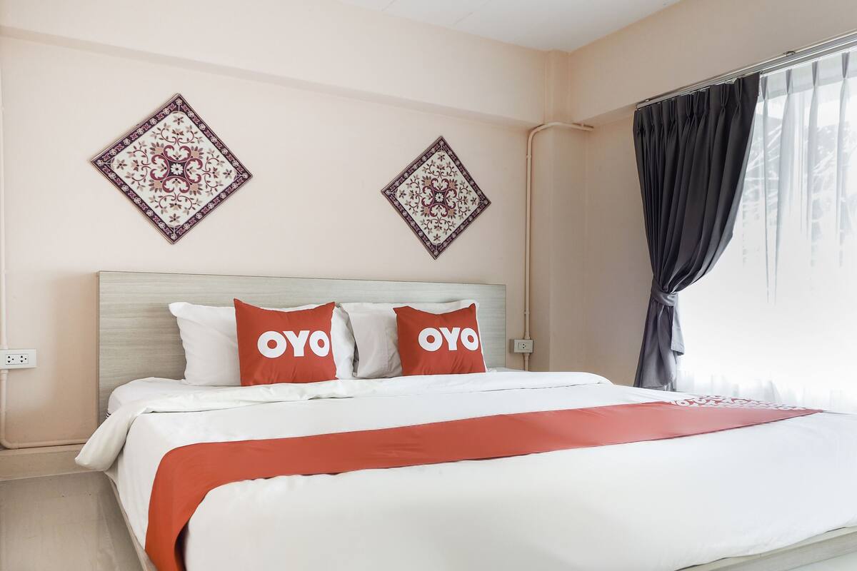 Une chambre d’hôtel comprenant un lit, deux oreillers à l’effigie de la marque « OYO », un plaid rouge et deux éléments de décoration murale.