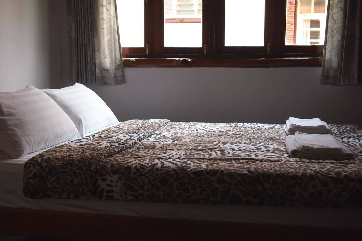 Ein Bett mit einer Bettdecke mit Leopardenmuster, weißen Kissen und gefalteten Handtüchern.