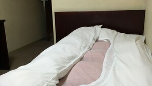 A single bed with white and pink bedding in a room with a plain wall and a wooden headboard. - Aoi Business Hotel (Fukuyama)
