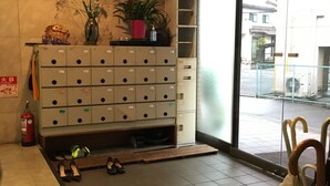 A hotel lobby with a shoe rack, a fire extinguisher, and a large window offering a view of the street. - Aoi Business Hotel (Fukuyama)