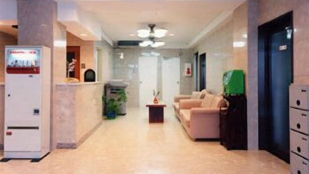 A hotel lobby with a reception desk, a seating area with sofas, a refrigerator, and a trash bin. - Aoi Business Hotel (Fukuyama)