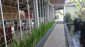 A pathway leading to a covered seating area with a view of a garden and a water feature. - K2 Eco Boutique Lombok (Mataram)