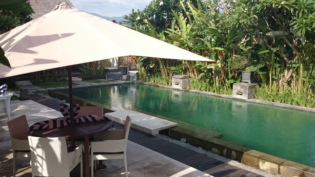 A poolside area with a table and chairs under a canopy, surrounded by lush greenery. - K2 Eco Boutique Lombok (Mataram)