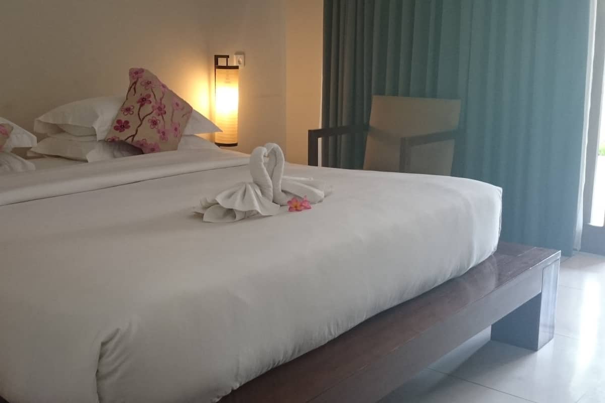 Ein Hotelzimmer mit einem großen Bett, weißen Leinen, blumigen Kissen, einer Nachttischlampe und Blick ins Freie.