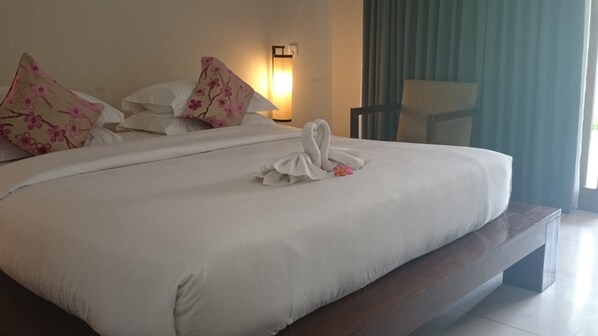 Habitación de hotel con una cama grande, ropa de cama blanca, almohadas estampadas con motivos florales, una lámpara de noche y vistas al exterior.