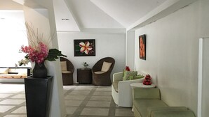 Un salon moderne avec un plafond haut, une grande fenêtre et une vue sur l’extérieur. On y trouve deux canapés, une table basse et une plante en pot.