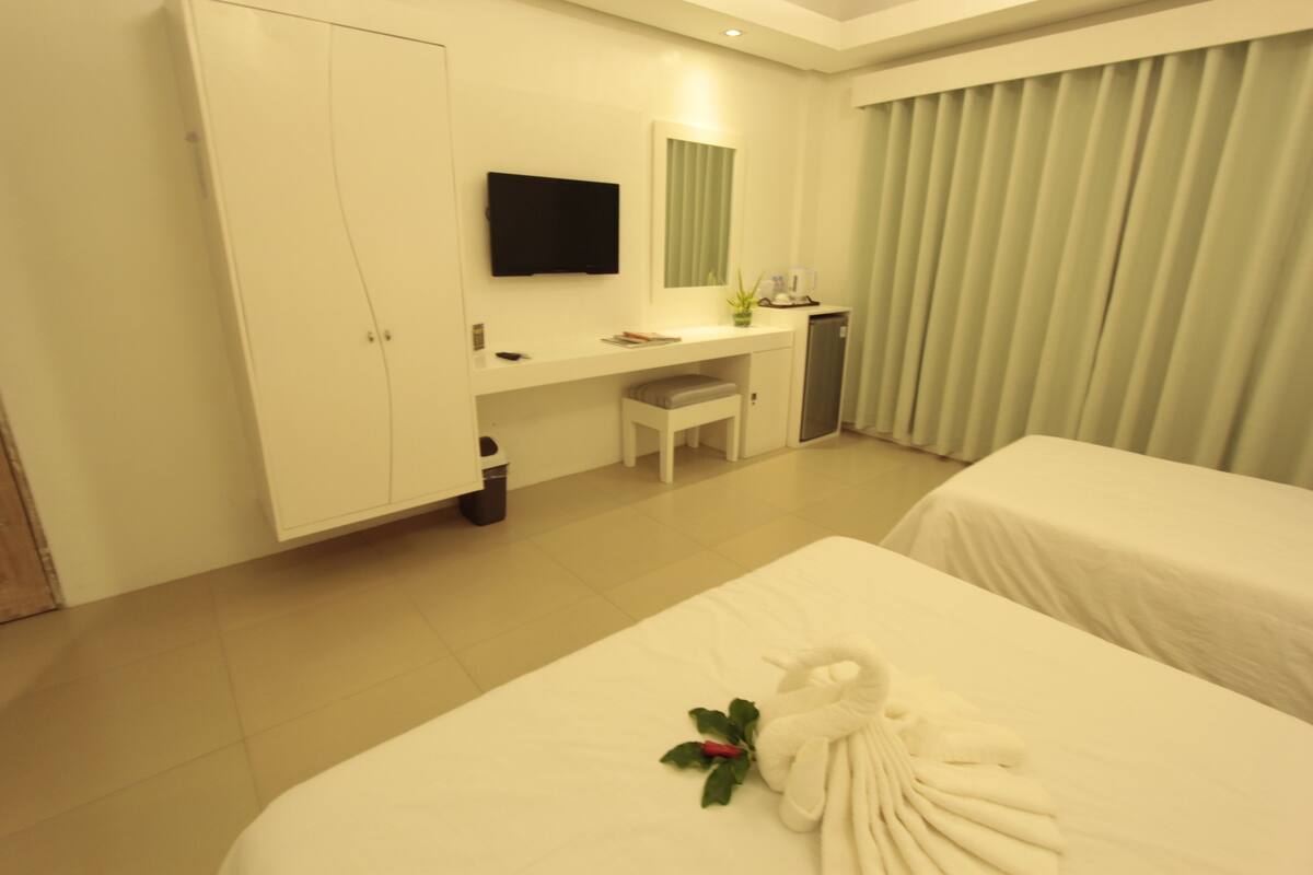 Une chambre d’hôtel avec un lit, un bureau, une télévision et une fenêtre avec des rideaux.