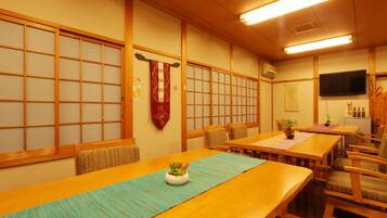 A traditional Japanese-style room with tatami mat flooring, wooden sliding doors, and a television mounted on the wall.