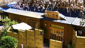 Un bâtiment traditionnel japonais, avec une enseigne, des clôtures en bois et des fleurs de cerisier.