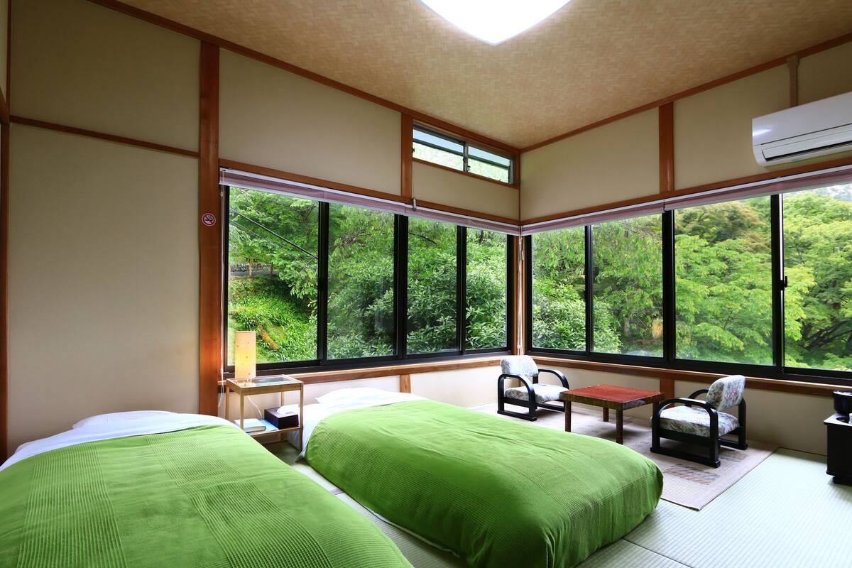 Una habitación con dos camas, una silla, una mesita y una ventana que ofrece vistas a zonas verdes.
