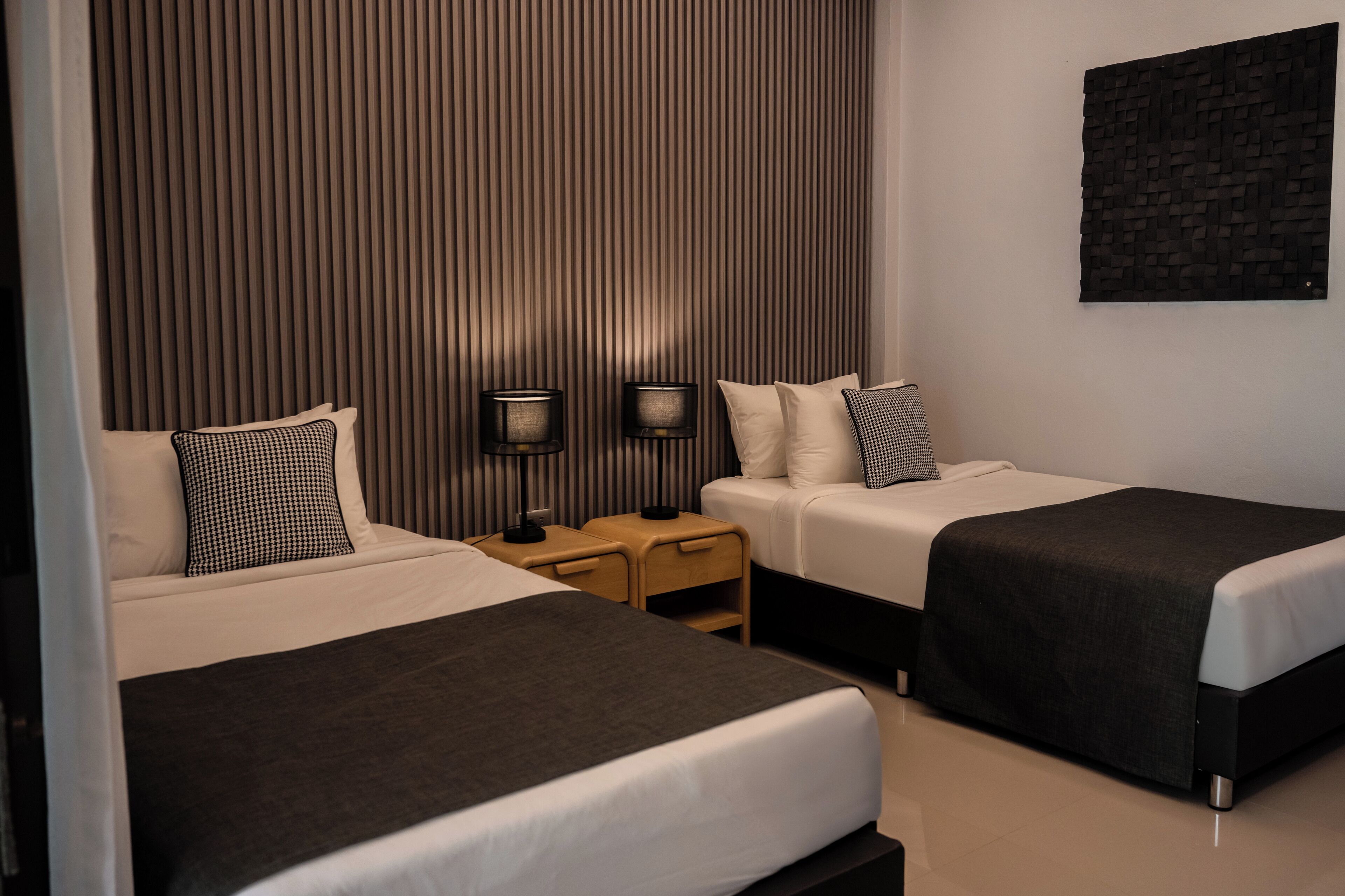 A hotel room with two beds, a nightstand, and a wall-mounted lamp.