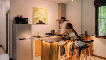 Une cuisine moderne équipée d’un réfrigérateur en acier inoxydable, d’un four à micro-ondes et d’un évier. Un tableau représentant des fleurs est accroché au mur, et une fenêtre offre une vue sur la verdure.