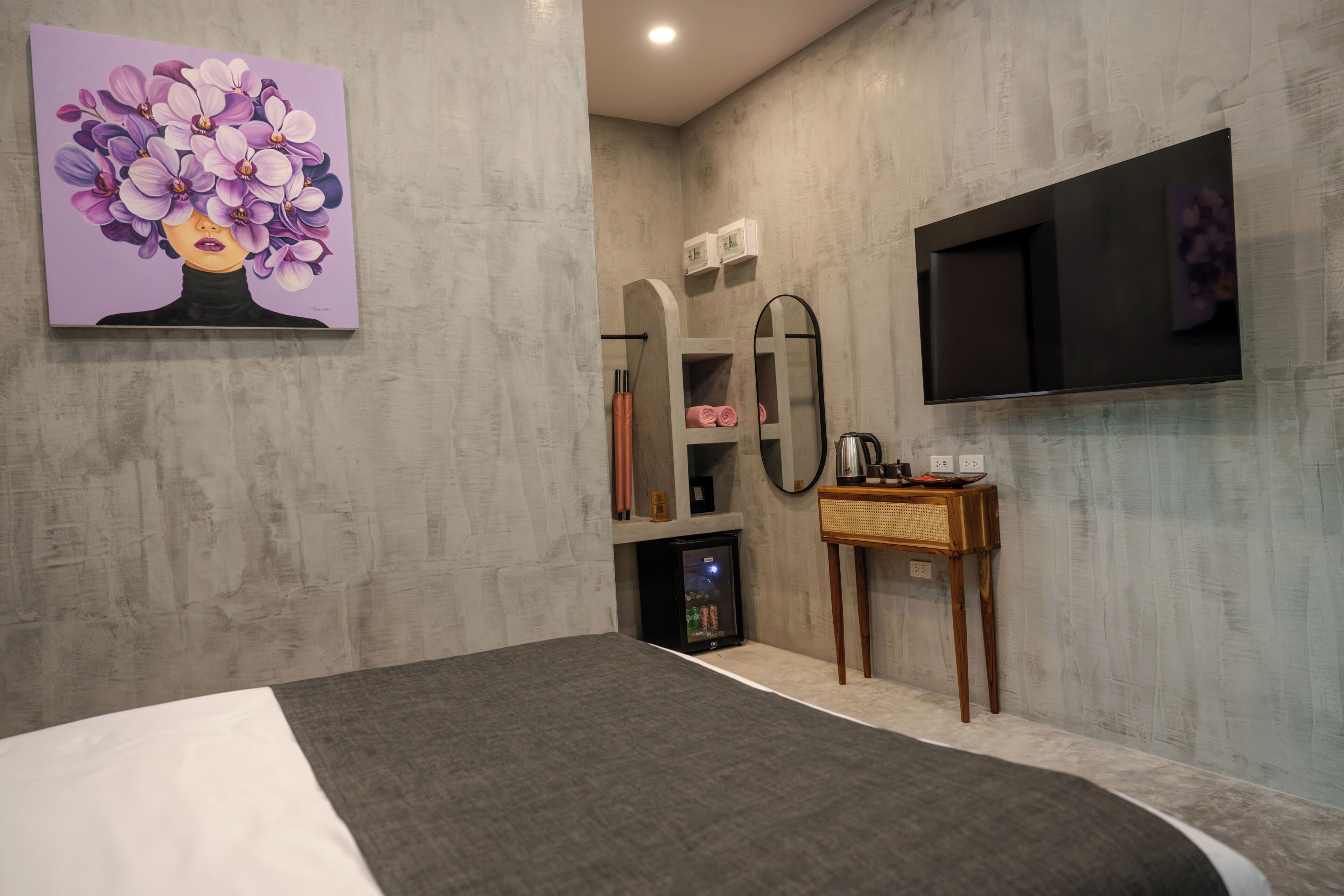 Une chambre moderne équipée d’un lit, d’un téléviseur à écran plat, d’un miroir et d’une petite table avec une bouilloire.