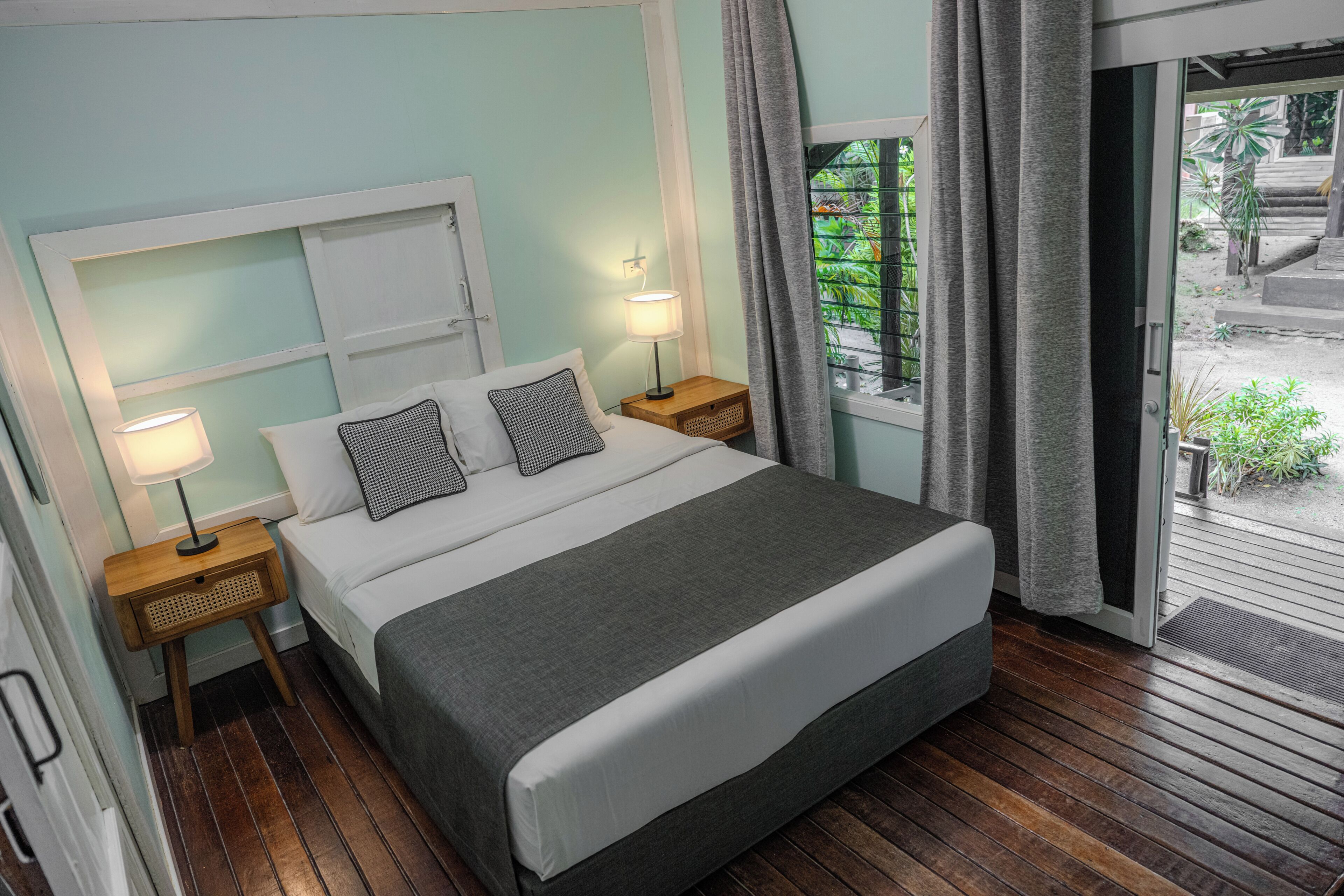 A bedroom with a bed, two bedside tables, a window with curtains, and a view of the outdoors.