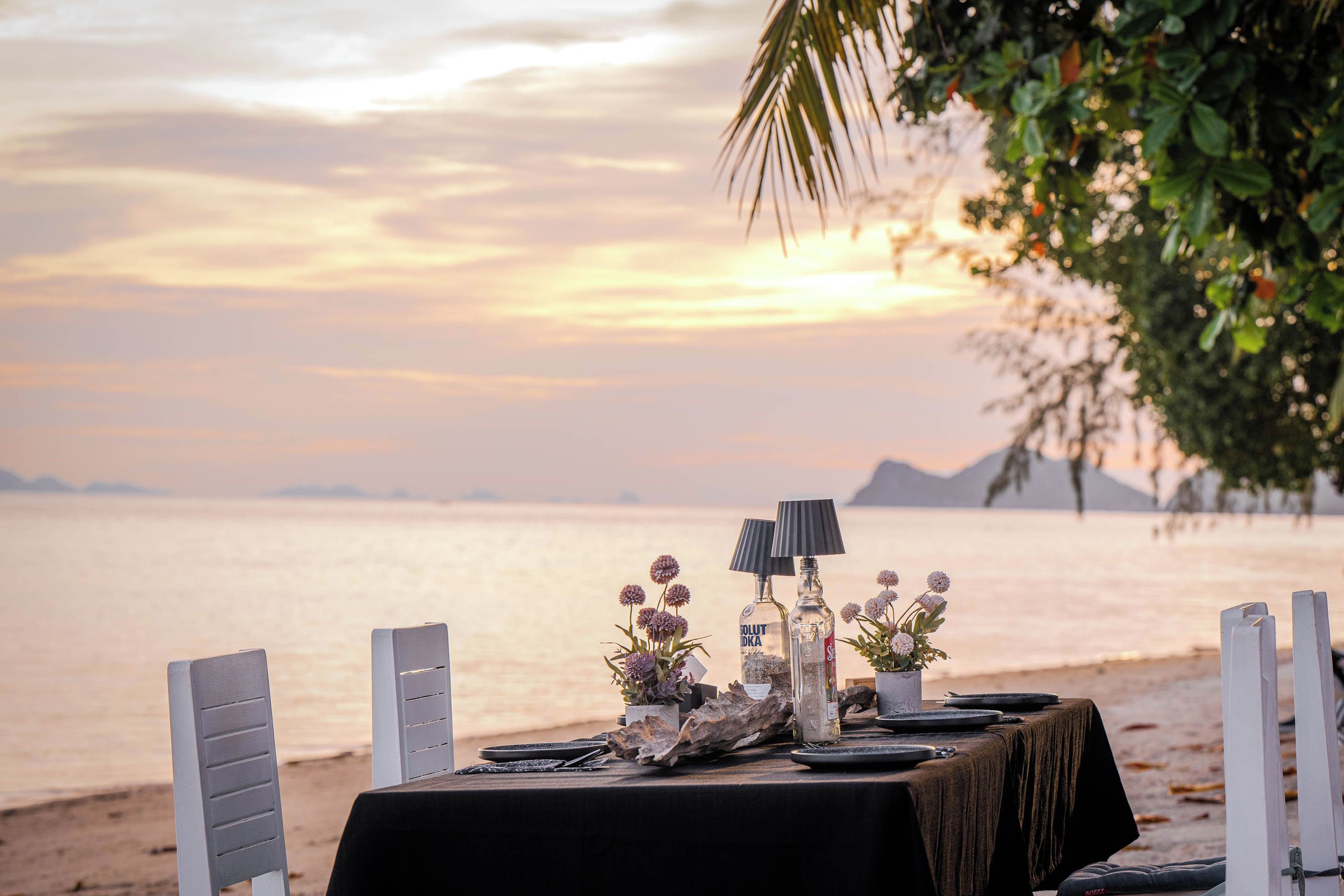 Una mesa preparada para una comida, con vista al mar y montañas al fondo.